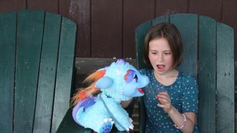 Youth sits in chair on porch with toy dragon.