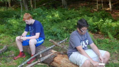 Youth shave the bark off of a log during a living history class. 