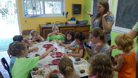 Counselor stands around a crowded table of youth painting rocks.