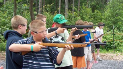 Campers taking aim with air rifles as others watch from behind.