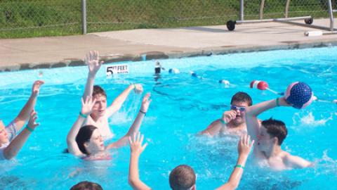 Group of campers in the pool trying to block a pass as another one tries to throw a ball to a teammate.