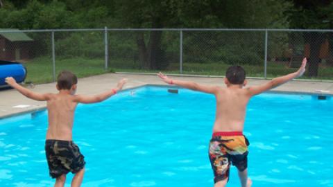 two young boys jumping into the pool simultaneously.