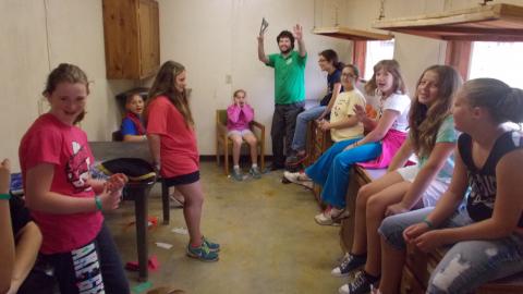group of youth sitting on a counter laughing with a counselor at the far end hands raised toward the camera.