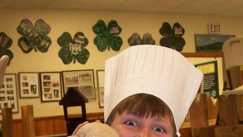 Camper wearing chef's hat and holding a ball of dough with grin on face