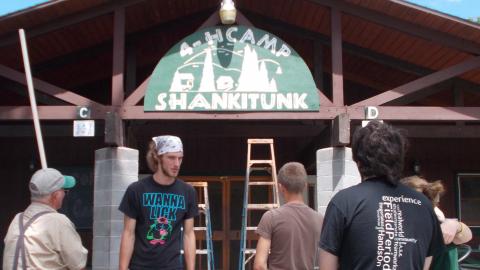 staff gathered together looking at the newly installed, hand-painted, 4-H Camp Shankitunk sign over Rice Dining Hall.