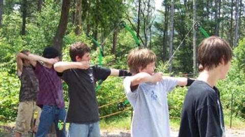 5 youth stand in a line with bows drawn ready to fire in archery class.