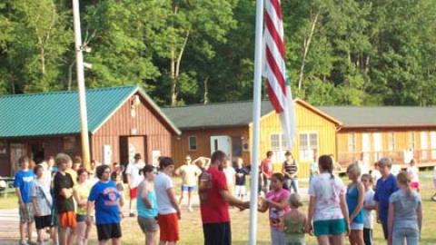 Campers stand gathered around the flagpole raising the flags up.