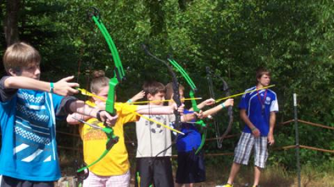 youth on the firing line draw their bow and prepare to fire their arrows as a counselor looks over the range.