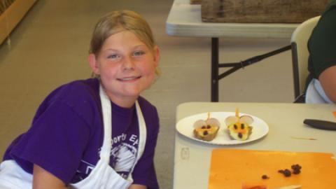 Camper smiling and sitting next to culinary creation.