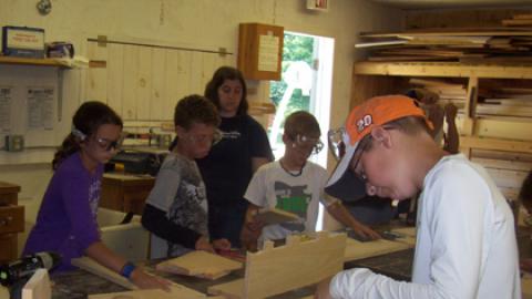 campers working on wooden bookshelves under the supervision of a counselor.
