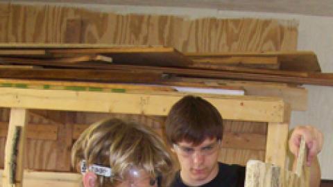 Youth working with counselor on large woodworking project.