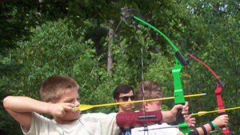 Campers draw their bow and prepare to fire while counselor looks on.