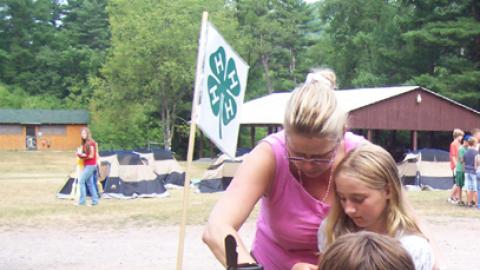 Craft Director works with two campers at a table.