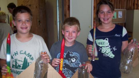 three youth holding soda bottle rockets and their painted model rocket.
