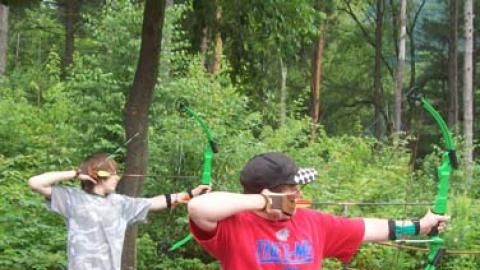 Two youth stand on the firing line with bows drawn.