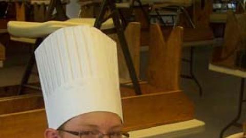teen in chef hat leaning back in chair smiling while holding up their parfait.