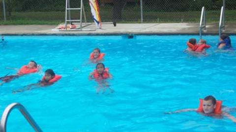 campers wearing life jackets in sparkling blue pool.
