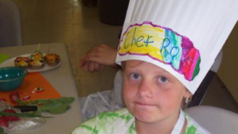 Camper wearing a chef's hat shows off culinary creation. 