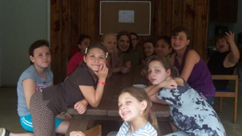 group of campers sitting at a table and looking to the camera during a class period.