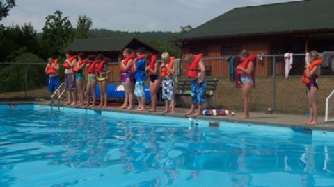 campers standing poolside with life jackets on.