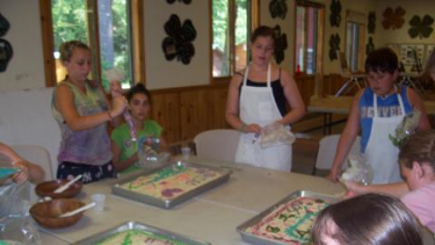 Campers decorate sheet cakes with colored frosting from pastry bags.