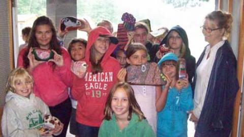 Group of campers smiling in doorway with craft director as they display newly painted rocks.