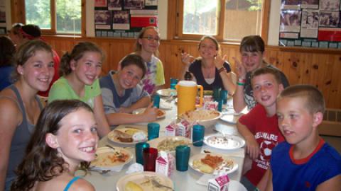 Table of smiling campers and counselors during a meal.