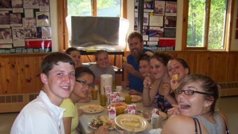 Table of smiling campers counselors during a meal.