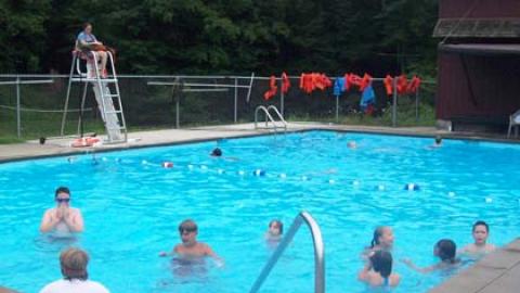 campers swimming in the pool while a lifeguard looks on from the deck.