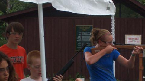 Youth takes aim with air rifle while two others charge their rifle.