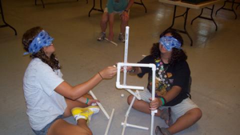 two blindfolded youth trying to build a tower from pvc pieces.