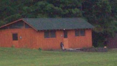 large cabin on meadows edge against wooded background.