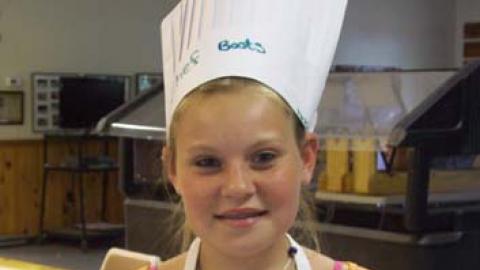Youth in paper chef hat displays culinary creation.