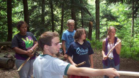 Youth stand with sticks on a hike through the woods. 