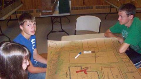 Three teens at table with large drawing of "Gumby Camp".