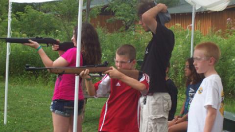 Youth take aim with air rifles from a standing position.