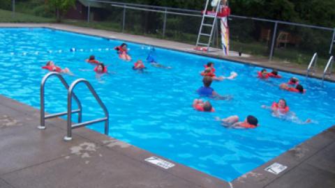distance view of campers swimming in pool deep end wearing life jackets.