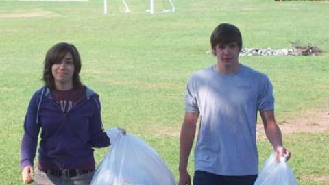 Two staff walk toward the camera, each carrying a bag of trash.