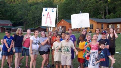 large group of campers huddled together and chanting with a picket sign "A" 