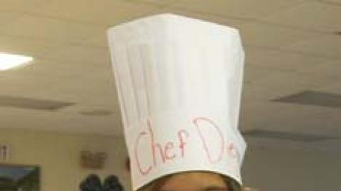 youth displaying a baked potato they made and wearing a paper chef hat.