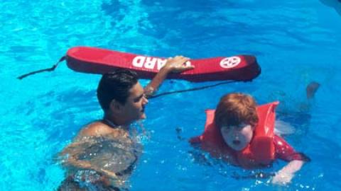 Lifeguard swims near youth wearing lifejacket.