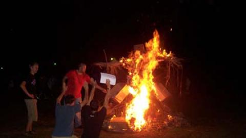 Counselors bow down in jest to a large bonfire.