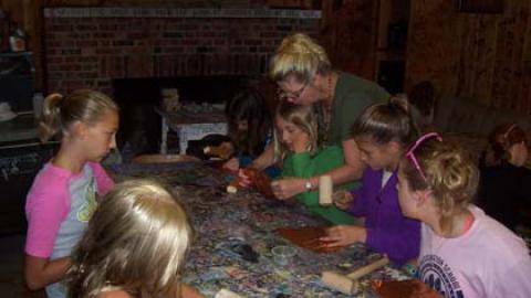 The Craft Director works with a group of youth gathered at a table to make foil creations.