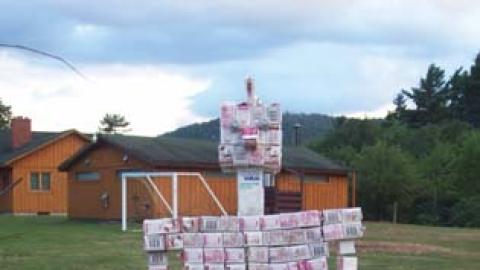 a man-like creation from used milk cartons stands next to the fire pit.