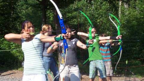 four youth in a line with bows drawn, ready to fire arrows under the watchful eye of their class counselor.