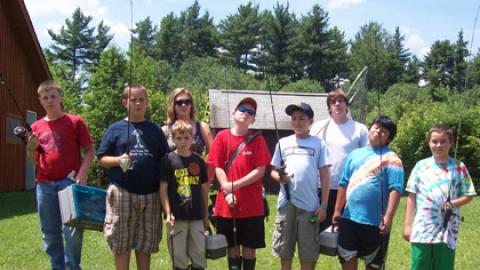 Group of youth with two counselors holding fishing poles and tackle boxes.