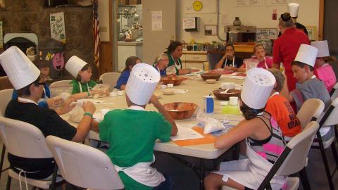 Youth sitting at a table wearing chef's hats. 