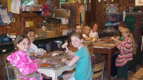 Youth sitting around tables in the craft hall with wooden mallets looking at camera and smiling.