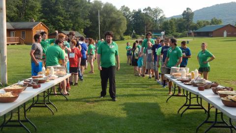 Campers and counselors line up to eat a meal outdoors. 