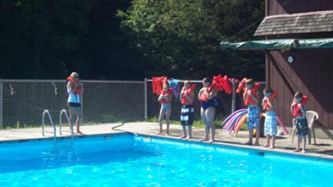 Youth standing on the side of the pool with life jackets waiting for swimming lessons. 